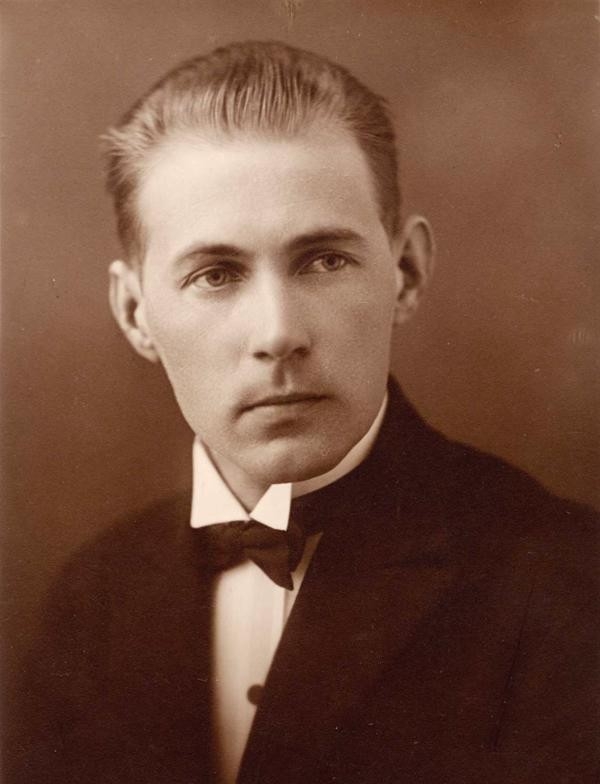 Senlaicīgs melnbalts jauna vīrieša portrets, formāli ģērbts, ar nopietnu sejas izteiksmi.