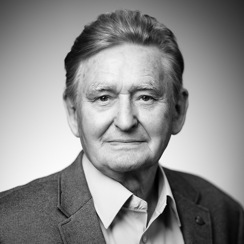 Melnbalta portreta fotogrāfijā gados vecāks cilvēks līdz krūtīm, skatienam vērstam pret kameru. Tērpts žaketē un kreklā.